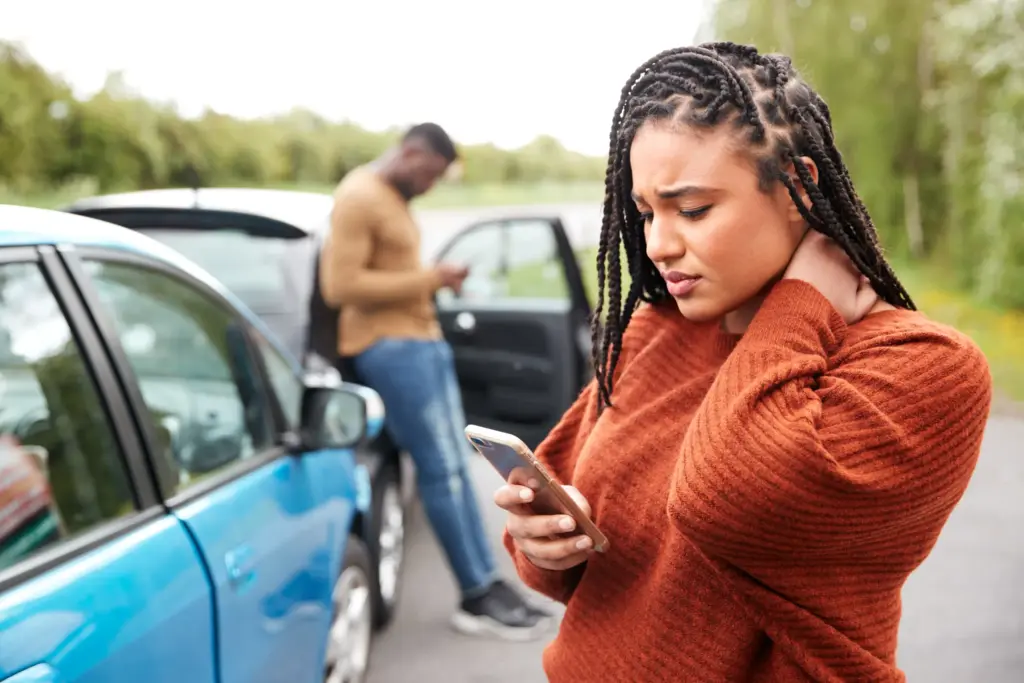 Mujer sosteniéndose el cuello junto a dos autos
