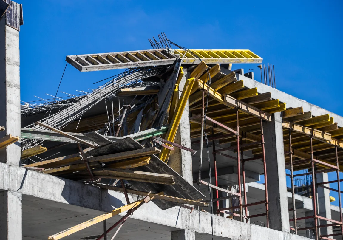 Partially collapsed concrete building under construction with exposed rebar and fallen scaffolding