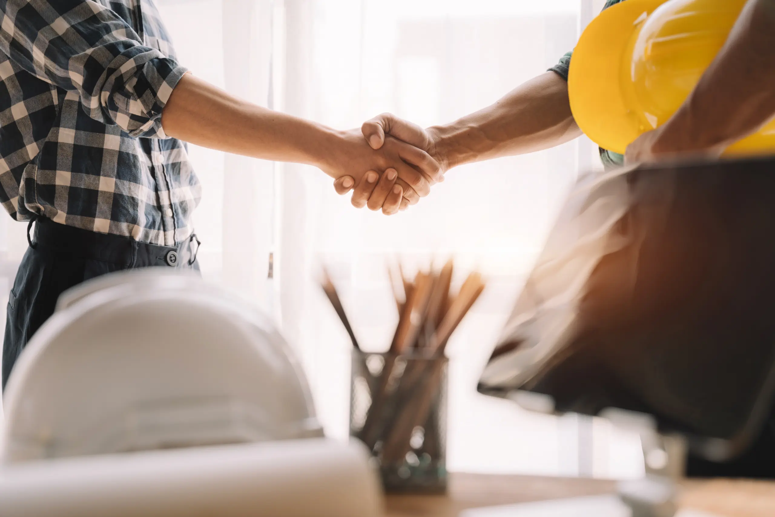 Two people shaking hands beside construction hard hats