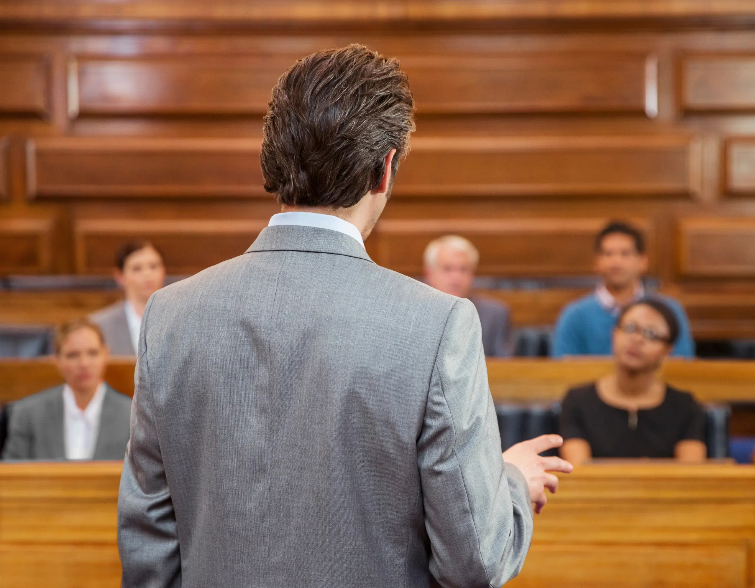 Man in a suit addressing seated people in a courtroom